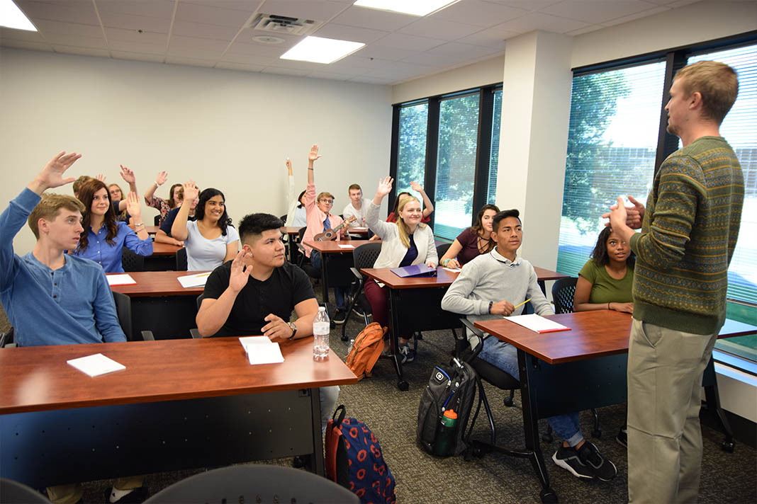 classroom with instructor at the front and kids hands in air